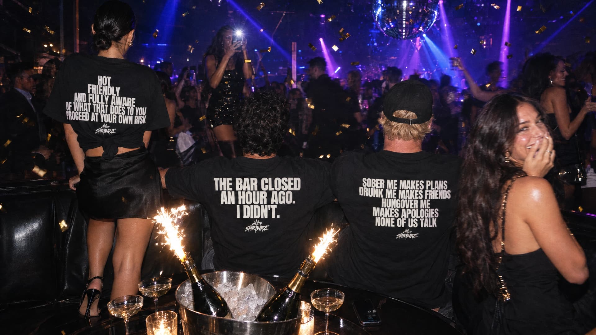 Friends in a nightclub booth with bottle service, seen from behind in black STRTWRZ tees with back prints